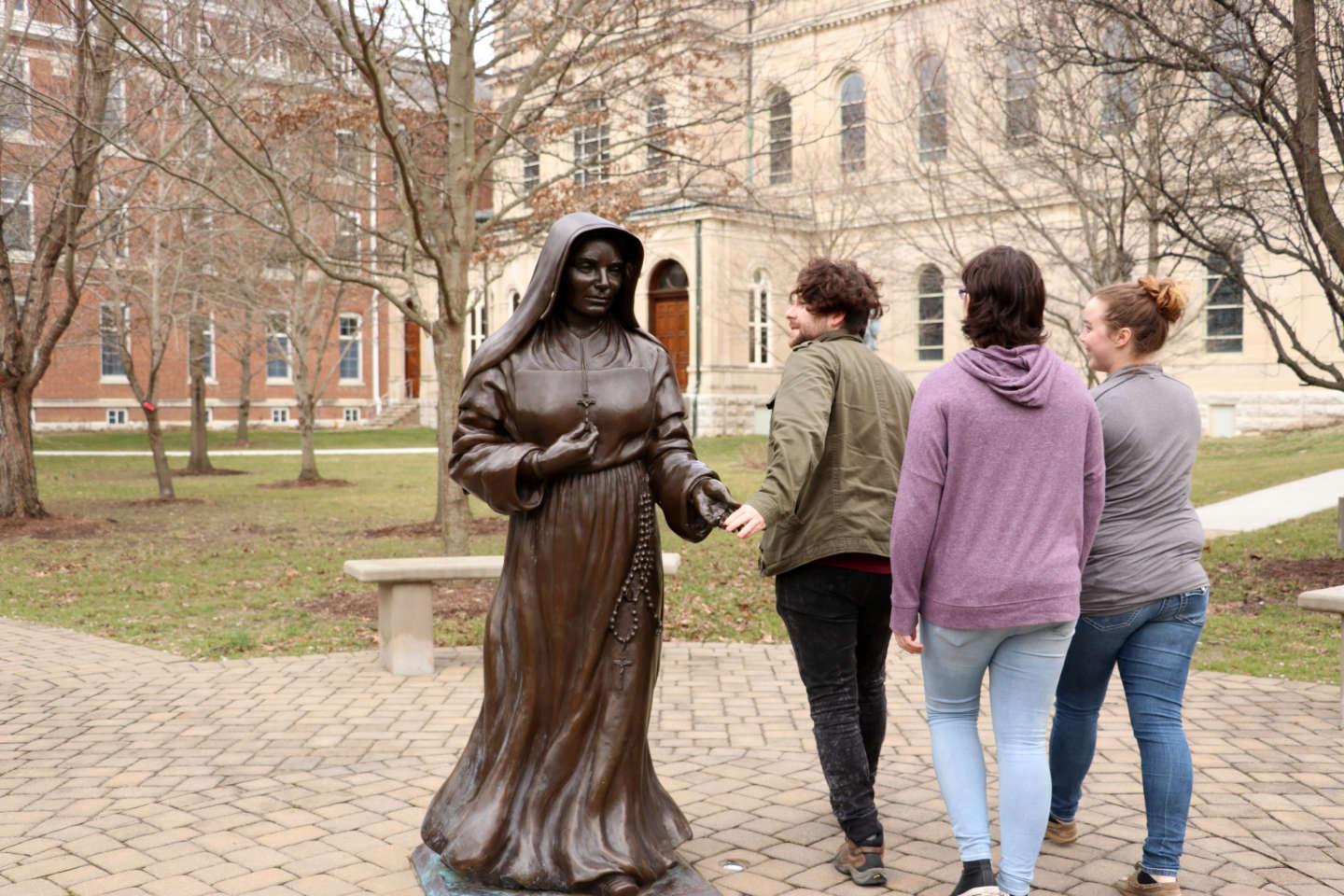 Students touch the hand of Saint Mother Theodore Guerin as they walk past the statue.